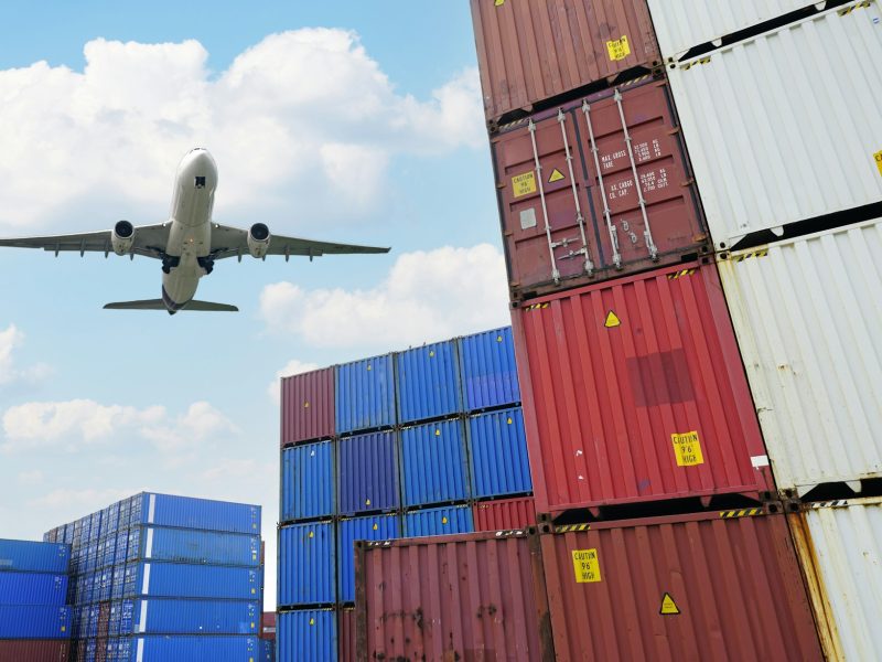 Cargo airplane flying above logistic container. Air logistic. Cargo and shipping business. Container